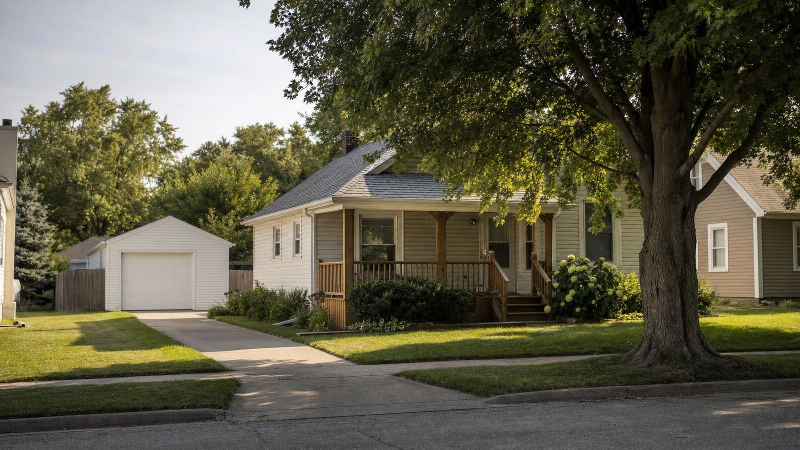 A well-kept single-story home with pale siding, a covered front porch and a swept concrete driveway on a shaded Kansas street